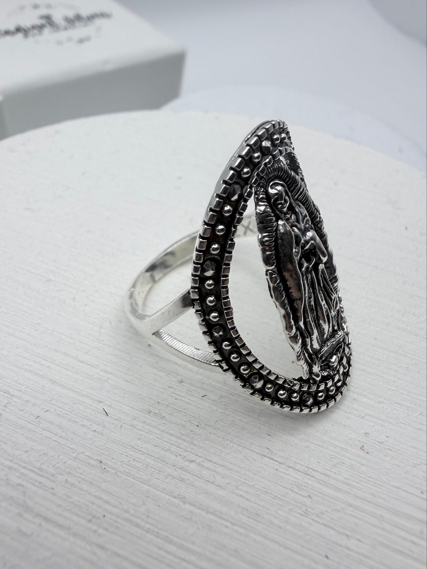 Silver ring with intricate design on a white stand
