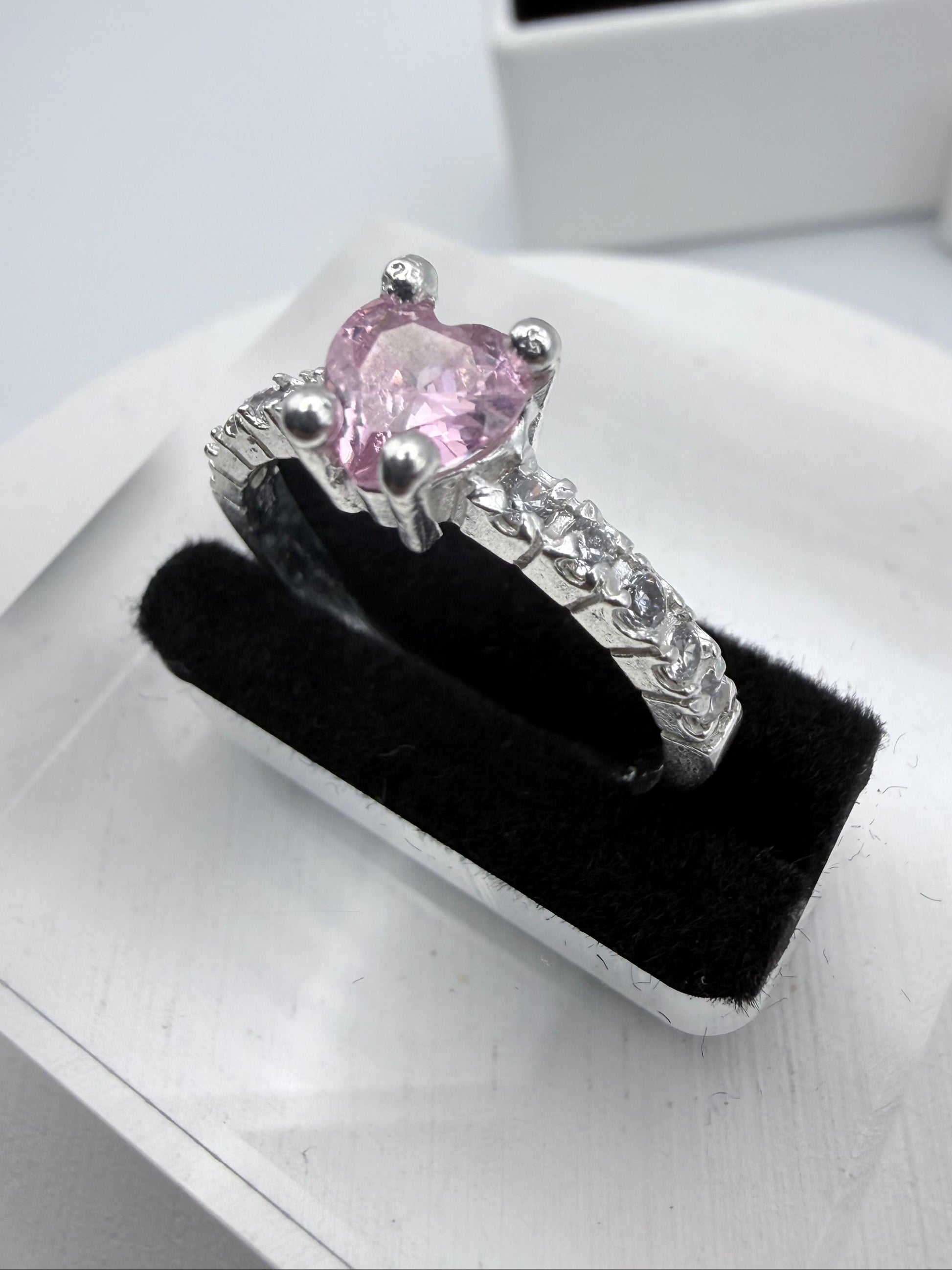 Silver ring with a pink gemstone on a black velvet stand against a white background