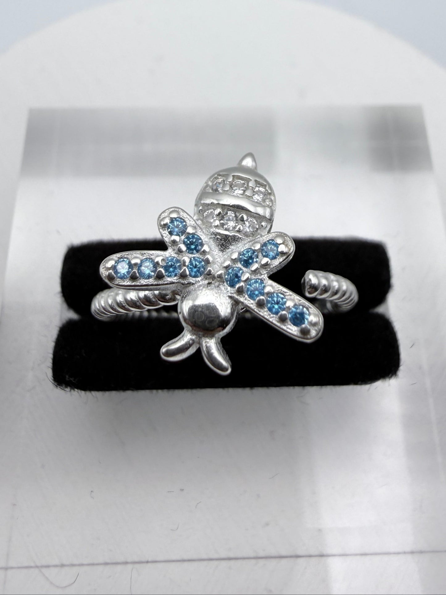 Silver bee-shaped jewelry piece with blue stones on a black background