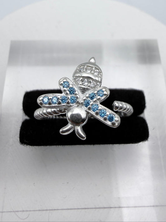 Silver bee-shaped jewelry piece with blue stones on a black background