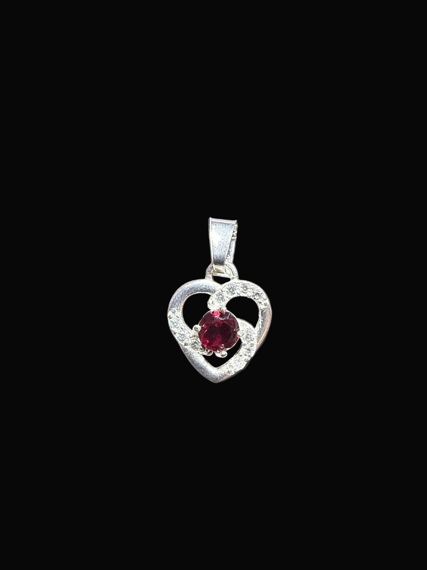 Heart-shaped silver earring with a red gemstone on a gray card.