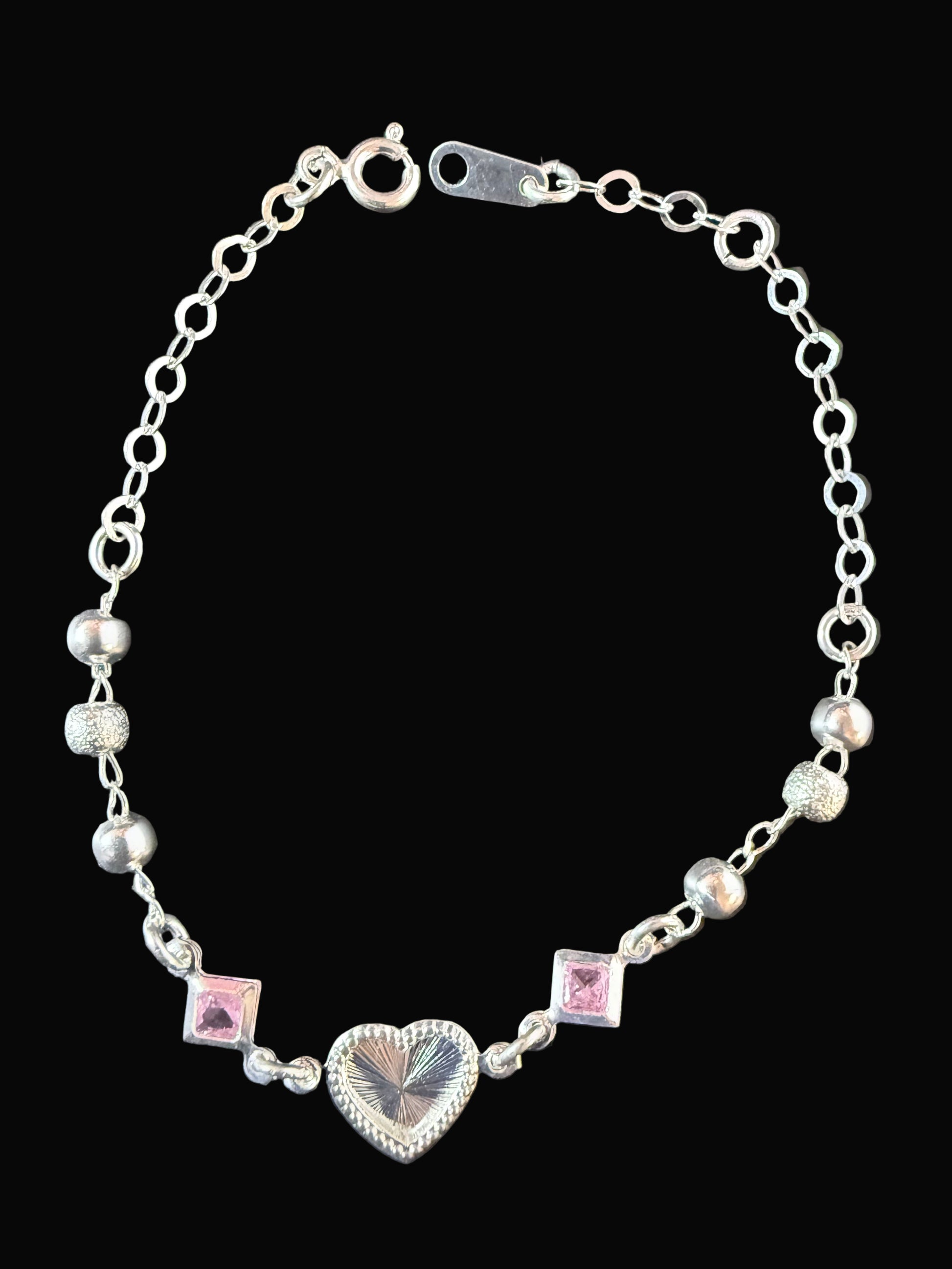 Silver bracelet with heart and square charms on a dark surface